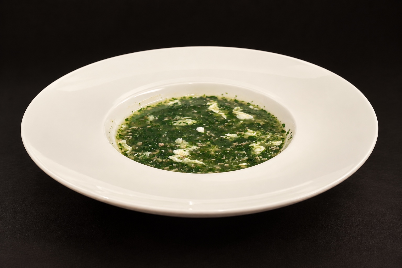 Potage à la caille et aux épinards dans une assiette creuse blanche